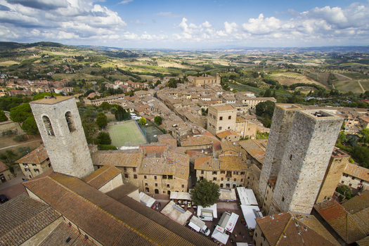 View of sun drenched towers piercing the skyline above terracotta rooftops nestled amidst rolling green hills and distant fields San Gimignano Tuscany Italy. View of sun drenched towers piercing the skyline above terracotta rooftops nestled amidst rolling green hills and distant fields San Gimignano Tuscany Italy.