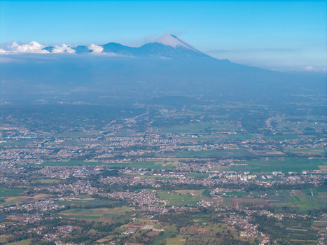 Aerial view of Mount Semeru rising above the city surrounded by lush green fields agricultural land and urban sprawl in Malang East Java Indonesia. Aerial view of Mount Semeru rising above the city surrounded by lush green fields agricultural land and urban sprawl in Malang East Java Indonesia.