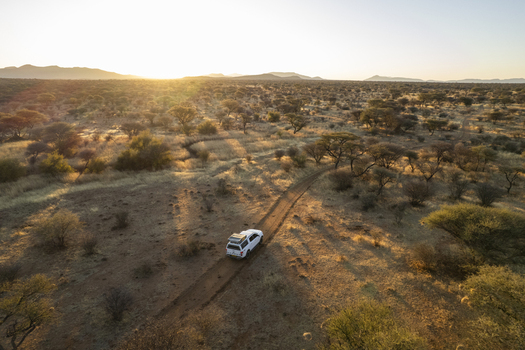 Aerial view of a lone white vehicle traversing a rugged dirt road through the vast sun kissed Namibian savanna Namibia. Aerial view of a lone white vehicle traversing a rugged dirt road through the vast sun kissed Namibian savanna Namibia.
