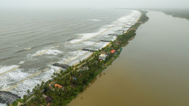 Aerial view of Mattu Beach a narrow strip of land separating the Arabian Sea from the backwaters featuring palm trees coastal houses and stone breakwaters in Udupi Karnataka India.