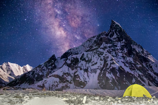 View of Mitre Peak under the Milky Way and starry night sky with a yellow tent on the snowy ground in Skardu Gilgit Pakistan.
