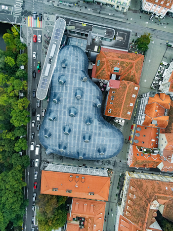 Aerial view of the Kunsthaus Graz a contemporary art museum with a distinctive blob like blue roof surrounded by historic red tiled rooftops and urban streets in Graz Styria Austria.