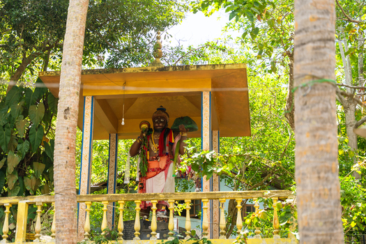 View of the colorful Hanuman statue holding a mountain within a yellow shrine surrounded by lush tropical greenery in Unawatuna Southern Province Sri Lanka. View of the colorful Hanuman statue holding a mountain within a yellow shrine surrounded by lush tropical greenery in Unawatuna Southern Province Sri Lanka.
