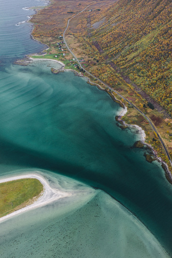 Aerial view of the Lofoten coastline featuring turquoise waters a sandy beach and a winding road along the autumn colored mountainside in Svolvaer Nordland Norway.