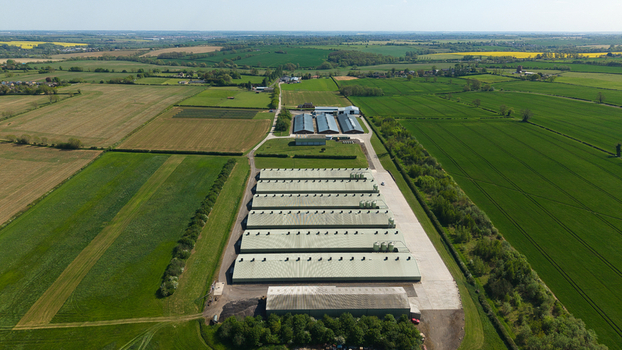 Aerial view of large industrial farm buildings and long agricultural sheds surrounded by vast green fields and rural landscape in Kettering England United Kingdom. Aerial view of large industrial farm buildings and long agricultural sheds surrounded by vast green fields and rural landscape in Kettering England United Kingdom.
