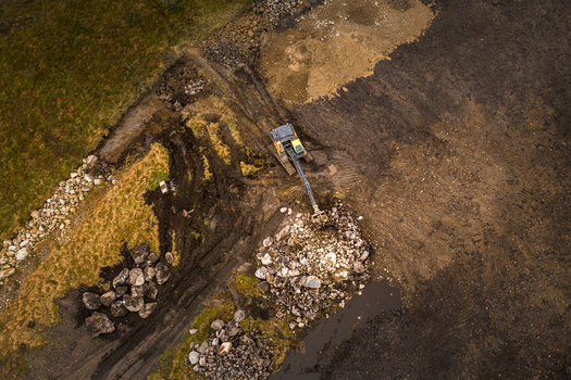 Aerial view of an excavator working in a field moving large rocks and clearing soil in the rural landscape of Jaeren Norway.