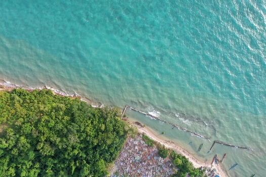 Aerial view of the coastline of Pulau Maginti featuring lush green forest a coastal cemetery and small wooden boats moored in the turquoise waters of Maginti South East Sulawesi Indonesia.