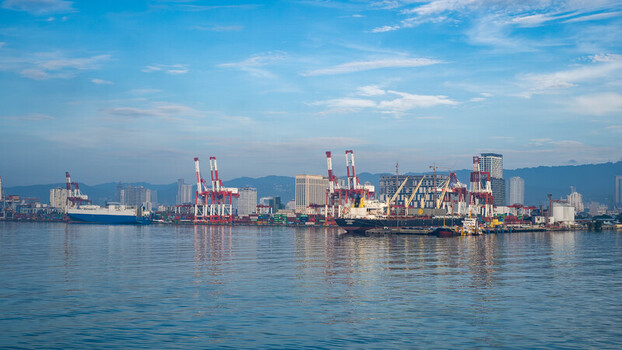 View of Cebu Port Authority with cargo ships container cranes and industrial infrastructure along the waterfront under a clear blue sky in Cebu City Central Visayas Philippines. View of Cebu Port Authority with cargo ships container cranes and industrial infrastructure along the waterfront under a clear blue sky in Cebu City Central Visayas Philippines.