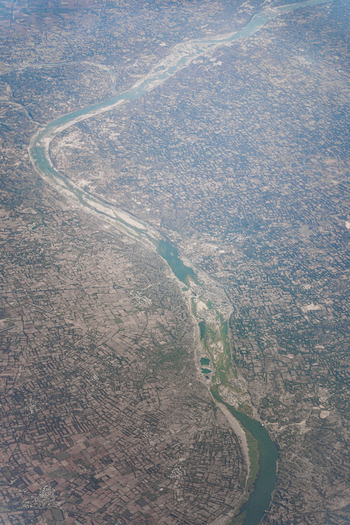 Aerial view of a winding river flowing through a vast landscape of agricultural fields and rural settlements in India. Aerial view of a winding river flowing through a vast landscape of agricultural fields and rural settlements in India.
