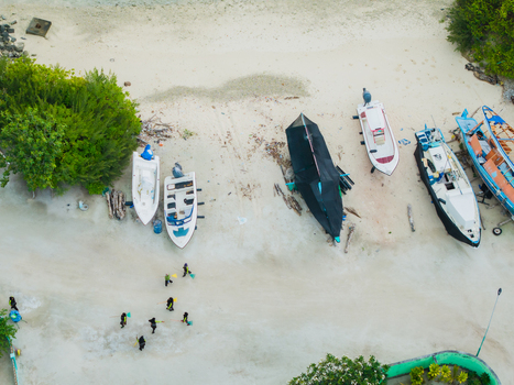 Aerial view of boats resting on the tranquil beach contrasting with the lush greenery and the crystal clear turquoise waters Vashafaru Island Maldives. Aerial view of boats resting on the tranquil beach contrasting with the lush greenery and the crystal clear turquoise waters Vashafaru Island Maldives.