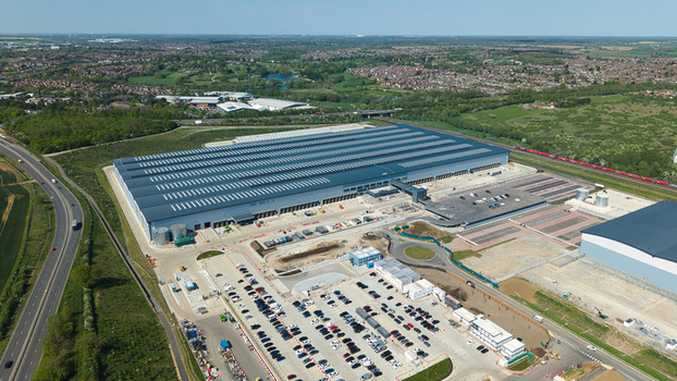 Aerial view of the large industrial warehouse at Symmetry Park with parking lots and surrounding green landscape under a clear blue sky in Kettering England United Kingdom. Aerial view of the large industrial warehouse at Symmetry Park with parking lots and surrounding green landscape under a clear blue sky in Kettering England United Kingdom.