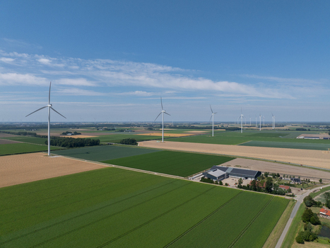 Aerial view of wind turbines standing in a vast rural landscape with green and golden agricultural fields under a clear blue sky in the Netherlands.