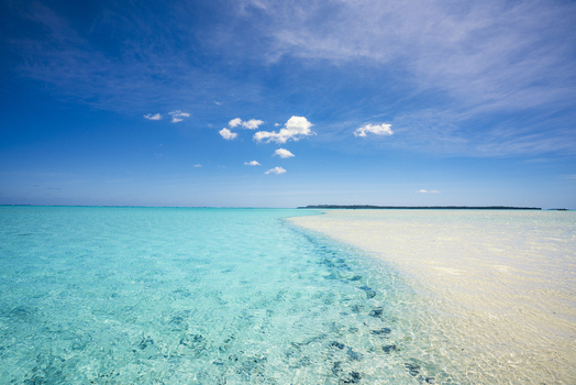 View of Aitutaki Lagoon with crystal clear turquoise water and a white sandbar under a bright blue sky in Aitutaki Cook Islands. View of Aitutaki Lagoon with crystal clear turquoise water and a white sandbar under a bright blue sky in Aitutaki Cook Islands.
