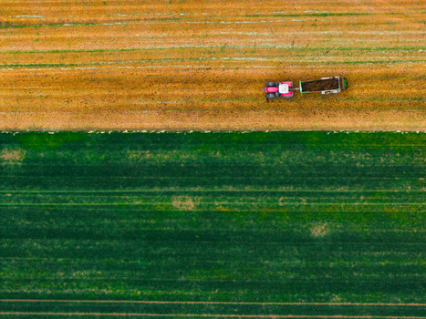 Aerial view of a tractor pulling a trailer across a field divided between brown soil and green crops in Cejkovice South Moravian Region Czechia.