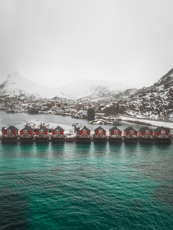 Aerial view of vibrant red cabins contrast against the turquoise sea and snow dusted mountains of Svolv&aelig;r Nordland Norway.