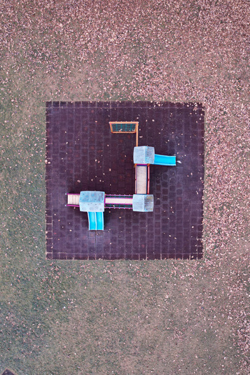 Aerial view of a colorful playground structure with blue slides on a dark square mat surrounded by autumn leaves in Turin Piedmont Italy. Aerial view of a colorful playground structure with blue slides on a dark square mat surrounded by autumn leaves in Turin Piedmont Italy.