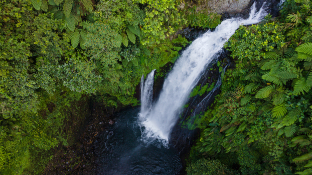 Aerial view of Gomblang Waterfall cascading through lush tropical forest and ferns in Kecamatan Kedungbanteng Jawa Tengah Indonesia. Aerial view of Gomblang Waterfall cascading through lush tropical forest and ferns in Kecamatan Kedungbanteng Jawa Tengah Indonesia.
