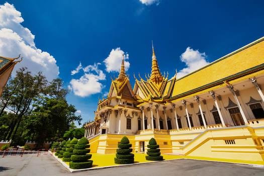 View of the Royal Palace of Cambodia featuring ornate yellow roofs and manicured topiary under a bright blue sky in Phnom Penh Phnom Penh Cambodia. View of the Royal Palace of Cambodia featuring ornate yellow roofs and manicured topiary under a bright blue sky in Phnom Penh Phnom Penh Cambodia.