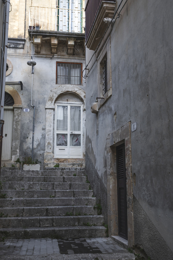 View of a narrow alleyway with stone steps and weathered historic building facades in Noto Sicily Italy. View of a narrow alleyway with stone steps and weathered historic building facades in Noto Sicily Italy.