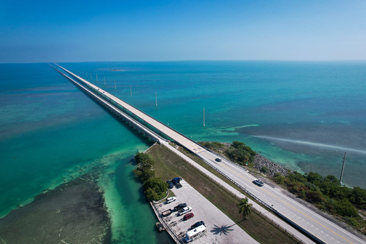 Aerial view of The Overseas Highway stretching across turquoise waters with cars driving along the bridge under a clear blue sky in Key Largo Florida United States. Aerial view of The Overseas Highway stretching across turquoise waters with cars driving along the bridge under a clear blue sky in Key Largo Florida United States.