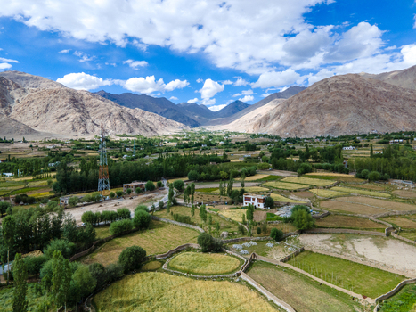 Aerial view of the Ladakh landscape with green fields stone walls trees and mountains under a blue sky in Ladakh Division Ladakh India. Aerial view of the Ladakh landscape with green fields stone walls trees and mountains under a blue sky in Ladakh Division Ladakh India.