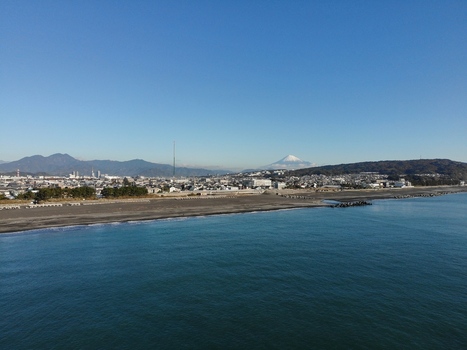 Aerial view of a coastal city with a dark sandy beach and Mount Fuji visible in the distance under a clear blue sky in Motobu Okinawa Japan. Aerial view of a coastal city with a dark sandy beach and Mount Fuji visible in the distance under a clear blue sky in Motobu Okinawa Japan.