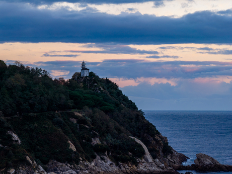 Aerial view of the lighthouse at Getariako portua perched on a lush cliffside overlooking the sea at dusk in Getaria Basque Country Spain. Aerial view of the lighthouse at Getariako portua perched on a lush cliffside overlooking the sea at dusk in Getaria Basque Country Spain.
