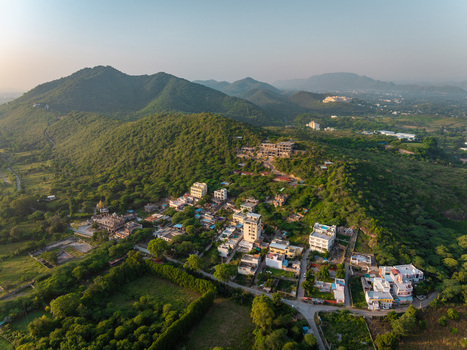 Aerial view of residential buildings nestled among lush green hills under a clear sky in Udaipur Rajasthan India.