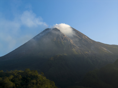 Aerial view of the smoking peak of Mount Merapi volcano with lush green slopes and a clear blue sky near Kecamatan Pakem Daerah Istimewa Yogya Indonesia. Aerial view of the smoking peak of Mount Merapi volcano with lush green slopes and a clear blue sky near Kecamatan Pakem Daerah Istimewa Yogya Indonesia.