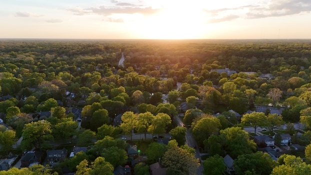 Aerial view of a lush green suburban neighborhood with residential houses nestled among dense trees during a golden sunset in Indianapolis Indiana USA. Aerial view of a lush green suburban neighborhood with residential houses nestled among dense trees during a golden sunset in Indianapolis Indiana USA.