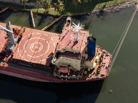 Aerial view of a cargo ship docked on the Rio Ozama with a winch area on the deck and a blue funnel near palm trees along the riverbank in Santo Domingo Santo Domingo Dominican Republic.