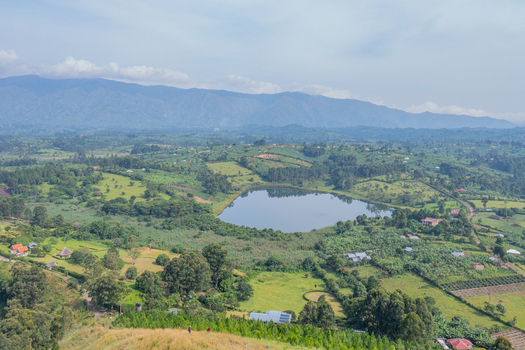 Aerial view of a serene crater lake surrounded by lush green hills scattered rural houses and dense vegetation in Fort Portal Western Region Uganda. Aerial view of a serene crater lake surrounded by lush green hills scattered rural houses and dense vegetation in Fort Portal Western Region Uganda.