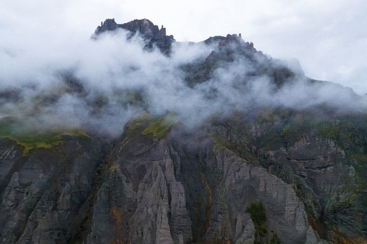 Aerial view of the rugged peaks of Mt. Sneffels shrouded in low hanging clouds above the rocky slopes and green alpine terrain of Yankee Boy Basin in Ouray Colorado United States.