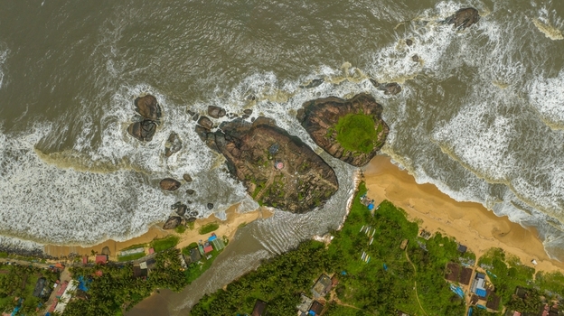 Aerial view of Kapu Light House situated on a rocky outcrop surrounded by the Arabian Sea with crashing waves and lush coastal vegetation in Udupi Karnataka India.