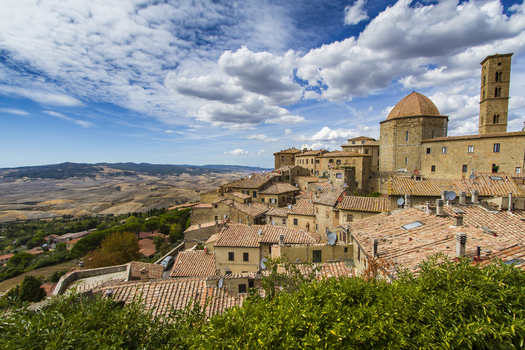 View of sun drenched rooftops cascading down the hillside towards the vast valley framed by lush greenery and ancient stone structures Volterra Tuscany Italy. View of sun drenched rooftops cascading down the hillside towards the vast valley framed by lush greenery and ancient stone structures Volterra Tuscany Italy.