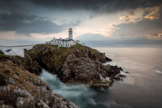 View of Fanad Head Lighthouse standing on rugged rocky cliffs under a dramatic cloudy sky in Baile Lair County Donegal Ireland.