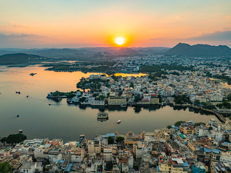 Aerial view of Udaipur the City of Lakes featuring historic architecture dense urban buildings and boats on Lake Pichola during a vibrant sunset. Udaipur Rajasthan India.