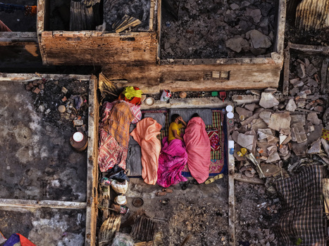 Aerial view of people sleeping on mats under colorful blankets amidst the debris of a burnt structure in Korail Basti Dhaka Dhaka Division Bangladesh.