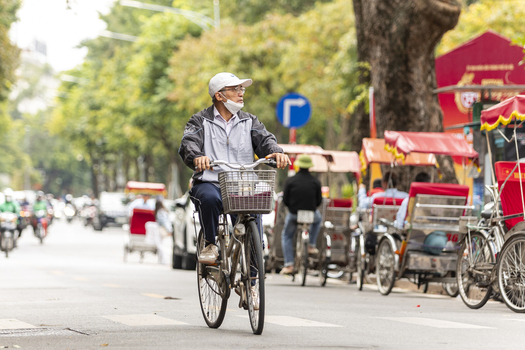 Hanoi Ha Noi Vietnam 11 November 2025 View of an elderly man cycling on a street in Hanoi with traditional cyclos parked along the roadside under lush trees.