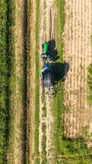 Aerial view of a green tractor pulling a reel irrigation system across a cultivated agricultural field in Milan Lombardy Italy. Aerial view of a green tractor pulling a reel irrigation system across a cultivated agricultural field in Milan Lombardy Italy.