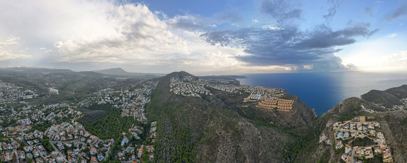 Aerial view of Moraira with residential villas nestled on green hills overlooking the Mediterranean Sea under a dramatic cloudy sky in Moraira Valencian Community Spain.