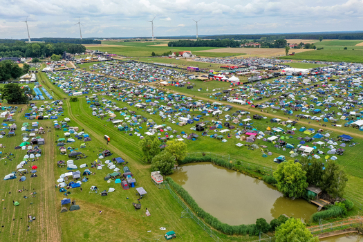 Aerial view of Open Beatz Festival campsite with numerous colorful tents people and wind turbines under a cloudy sky Herzogenaurach Bayern Germany. Aerial view of Open Beatz Festival campsite with numerous colorful tents people and wind turbines under a cloudy sky Herzogenaurach Bayern Germany.