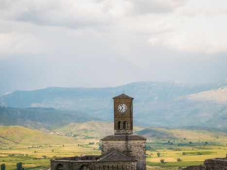 Aerial view of the historic stone clock tower of Gjirokaster Castle overlooking the green valley and rugged mountains under a cloudy sky Gjirokaster Gjirokaster County Albania. Aerial view of the historic stone clock tower of Gjirokaster Castle overlooking the green valley and rugged mountains under a cloudy sky Gjirokaster Gjirokaster County Albania.