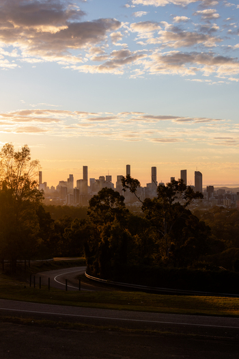 View of the Brisbane skyline at sunrise with silhouettes of trees and a winding road in the foreground in Brisbane Queensland Australia. View of the Brisbane skyline at sunrise with silhouettes of trees and a winding road in the foreground in Brisbane Queensland Australia.