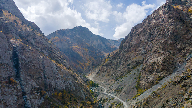 Aerial view of Deosai Top featuring a winding road through a rugged mountain valley with rocky slopes and autumn foliage under a blue sky in Skardu Gilgit Pakistan.
