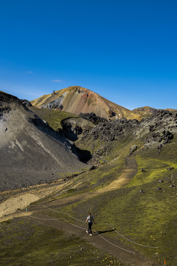 View of a solitary figure hiking amidst the vibrant otherworldly landscape of mossy greens volcanic blacks and rust colored mountains Rang&aacute;r&thorn;ing ytra Iceland.