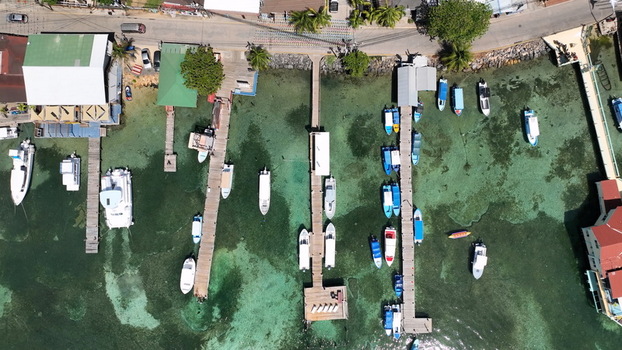 Aerial view of West End marina with various boats docked at wooden piers surrounded by clear turquoise water and coastal buildings in West End Bay Islands Department Honduras. Aerial view of West End marina with various boats docked at wooden piers surrounded by clear turquoise water and coastal buildings in West End Bay Islands Department Honduras.