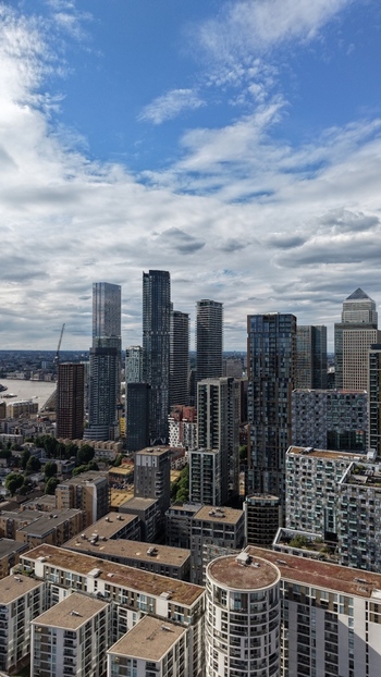 London United Kingdom 16 June 2026 Aerial view of Canary Wharf financial district featuring modern skyscrapers residential blocks and the River Thames under a cloudy sky.