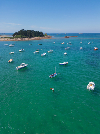 Aerial view of numerous small boats anchored in turquoise waters near the Plage de Port Blanc and a small forested island under a clear blue sky in Penvenan Bretagne France. Aerial view of numerous small boats anchored in turquoise waters near the Plage de Port Blanc and a small forested island under a clear blue sky in Penvenan Bretagne France.