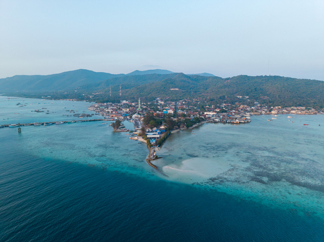 Aerial view of Karimunjawa Town Square surrounded by coastal buildings turquoise waters and lush green hills in Karimunjawa Central Java Indonesia. Aerial view of Karimunjawa Town Square surrounded by coastal buildings turquoise waters and lush green hills in Karimunjawa Central Java Indonesia.